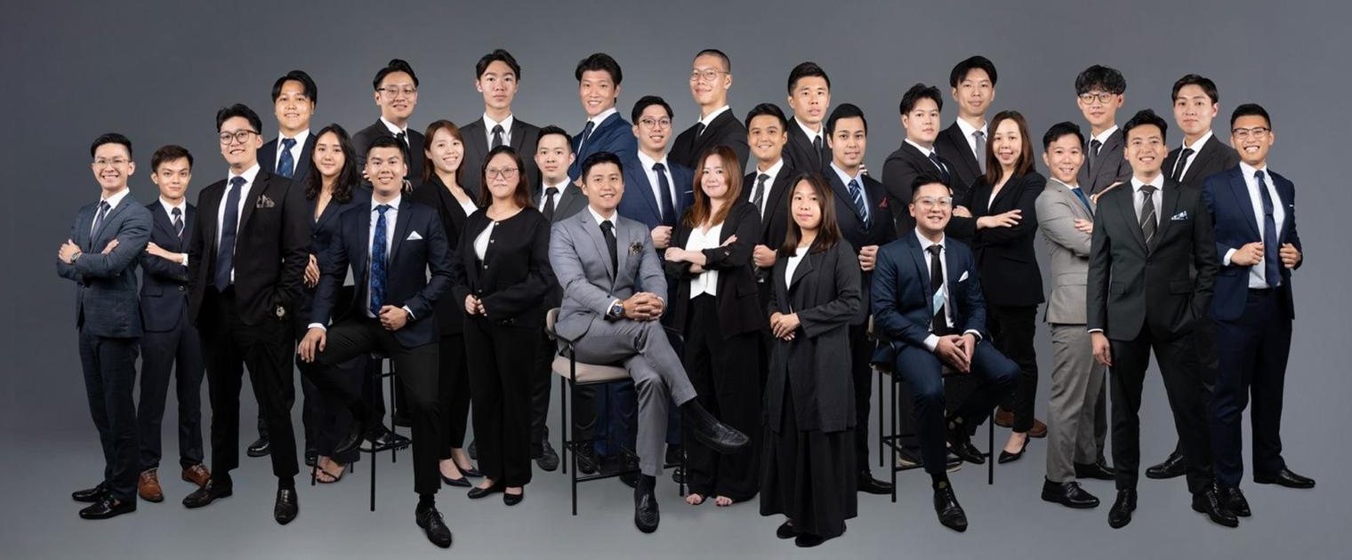 The Jonas Ng Organisation team, about twenty advisers in suits, posed together against a grey studio backdrop